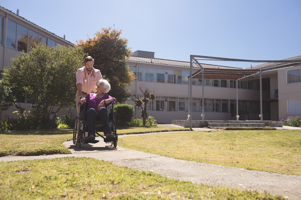Front view of male Caucasian doctor talking with disabled senior patient women in wheelchair against a retirement in background
