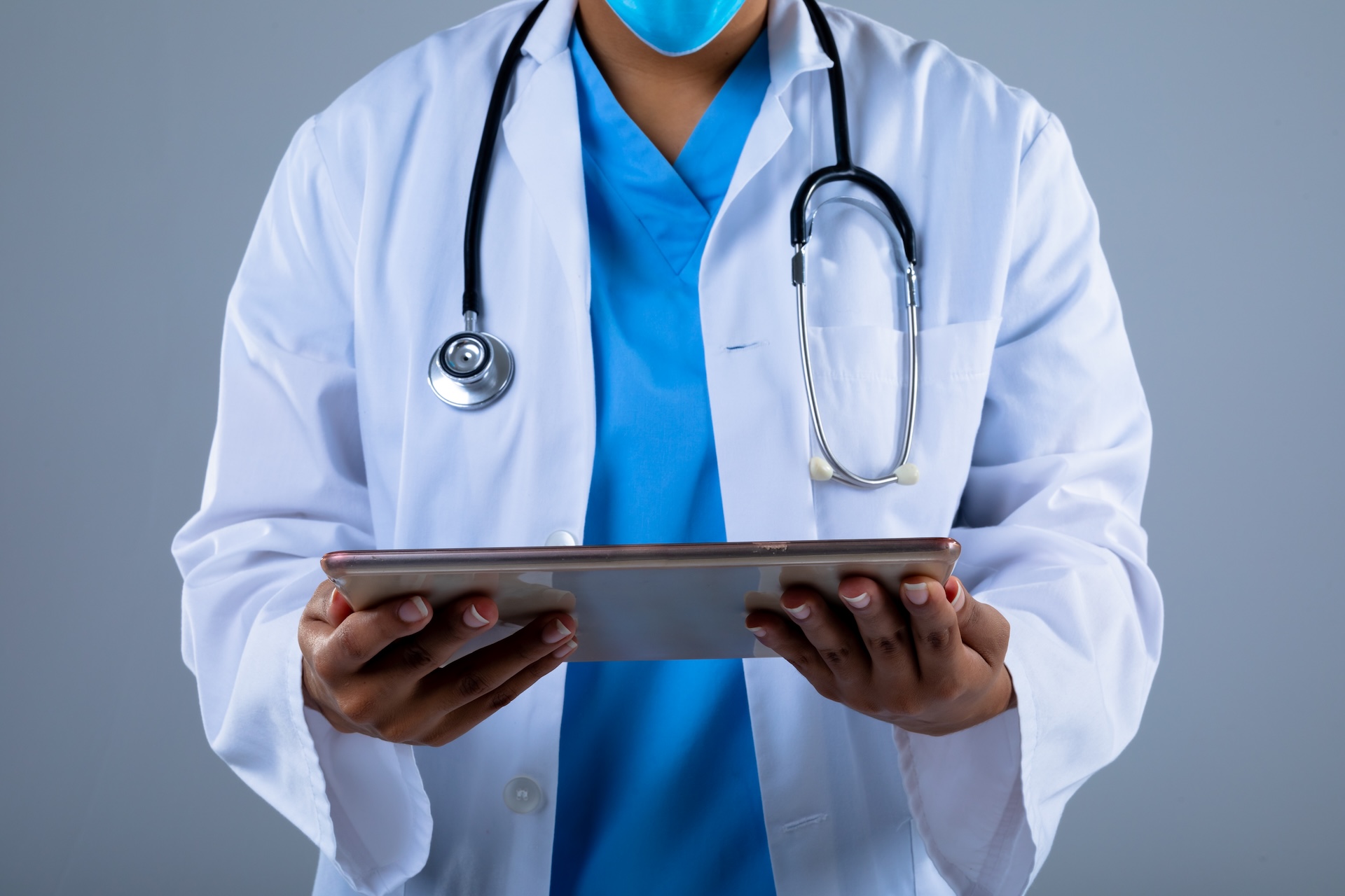 Mid section of female doctor holding digital tablet against grey background. healthcare and medical professionalism concept